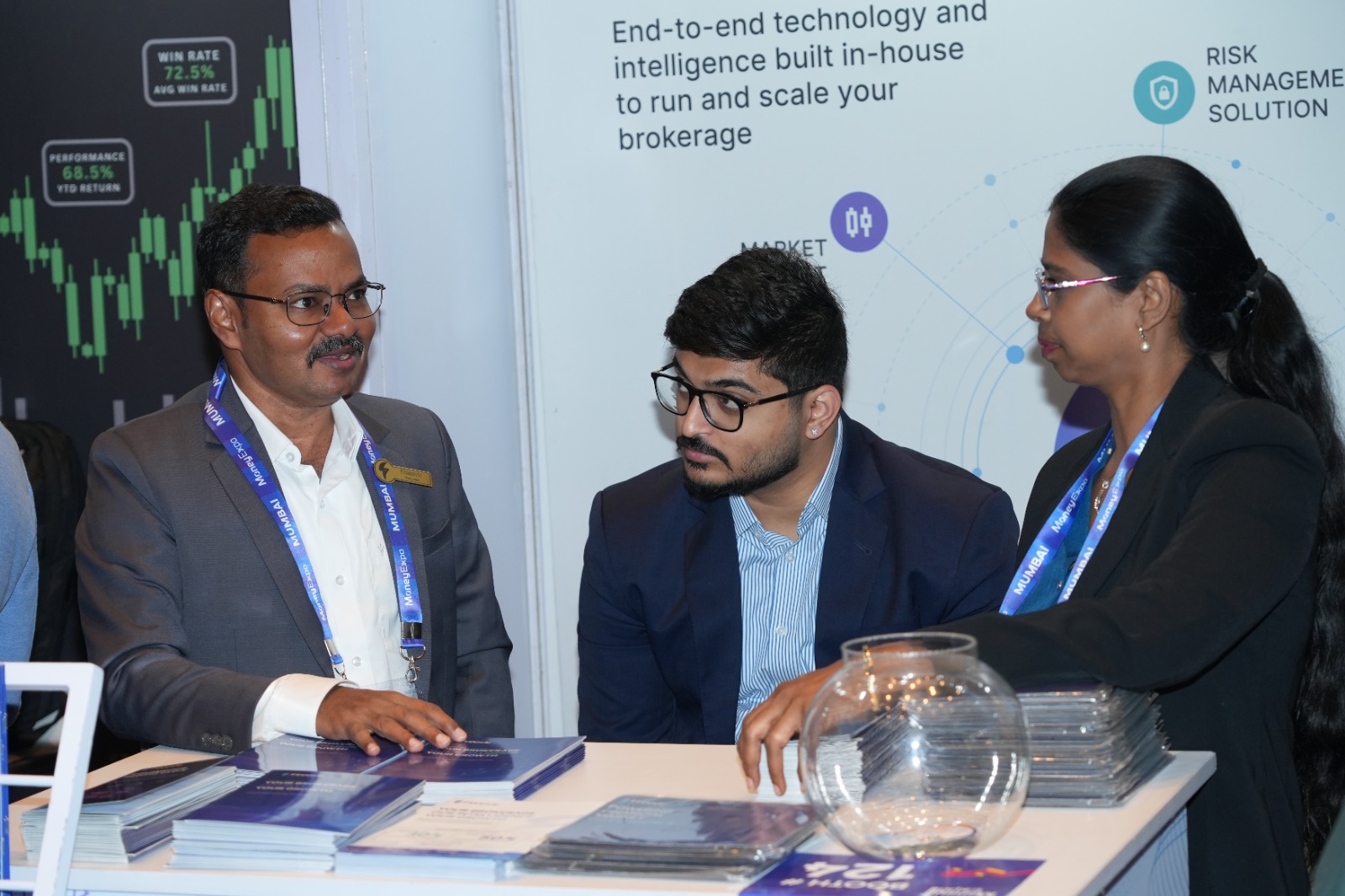 Two Finnovic team members talking broker technology with a visitor across the stand counter at Money Expo India 2026